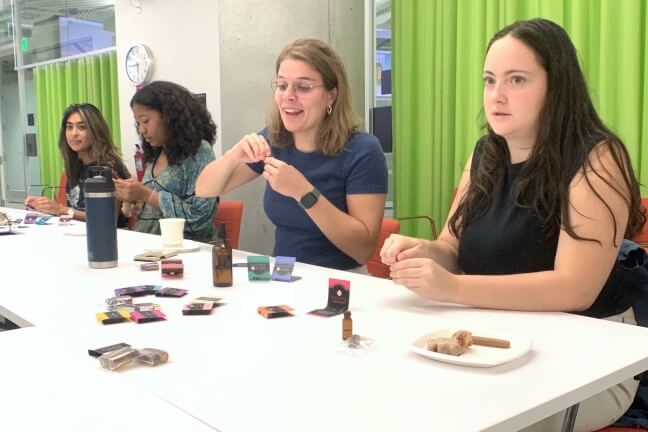 Students combining perfume samples and ingredients while seated at a white table