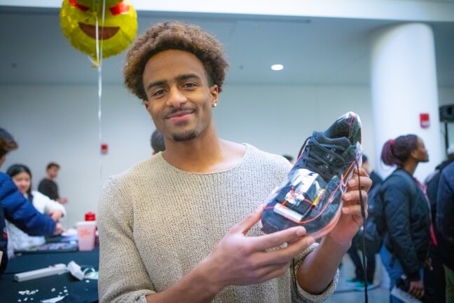 A male Harvard student holding up a sneaker at a computer science festival in Cambridge