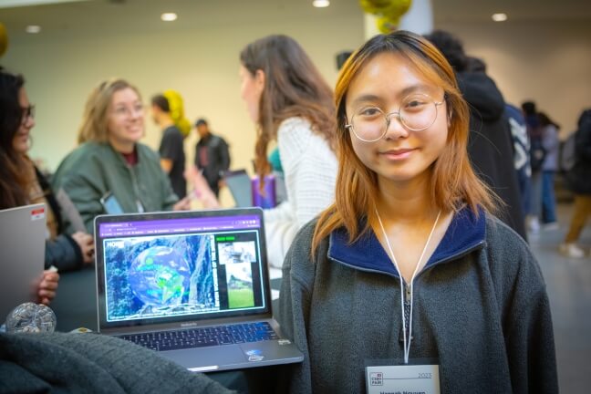 A female Harvard student next to a laptop displaying a virtual globe of the Earth