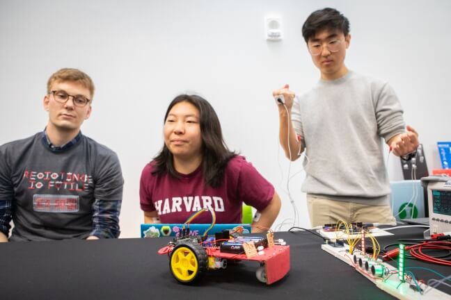 Three Harvard students sitting behind a toy car controlled by muscle flexion