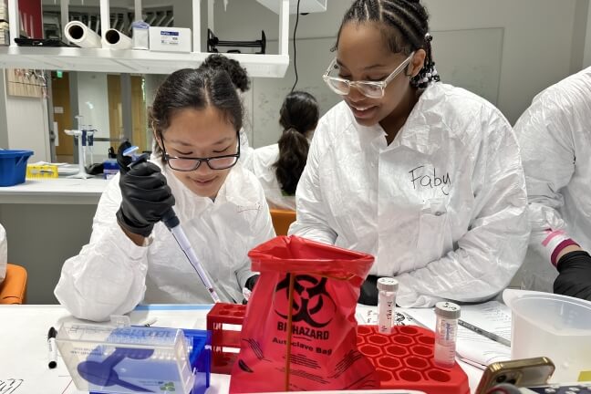 High school students Tenzinsherab Bachantsang and Fabiana Gomes holding micropipettes above a lab table