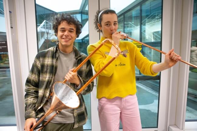 Two Harvard students holding musical instruments made from copper tubing