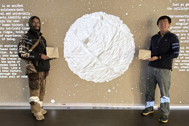 A Harvard student and MIT student holding 3D-printed blocks in front of a digitally projected image of a planet