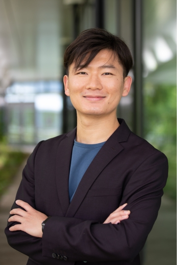 A man in a blue shirt and black blazer poses with his arms crossed. 