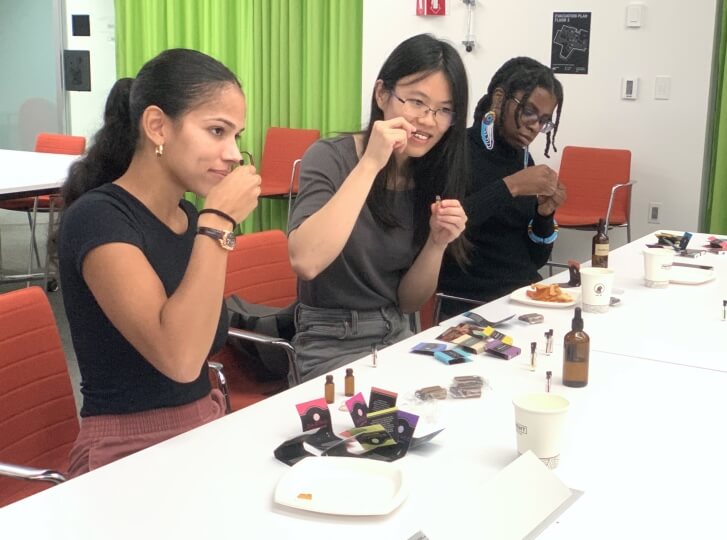 Three Harvard students smelling perfume samples and ingredients, sitting next to a white table