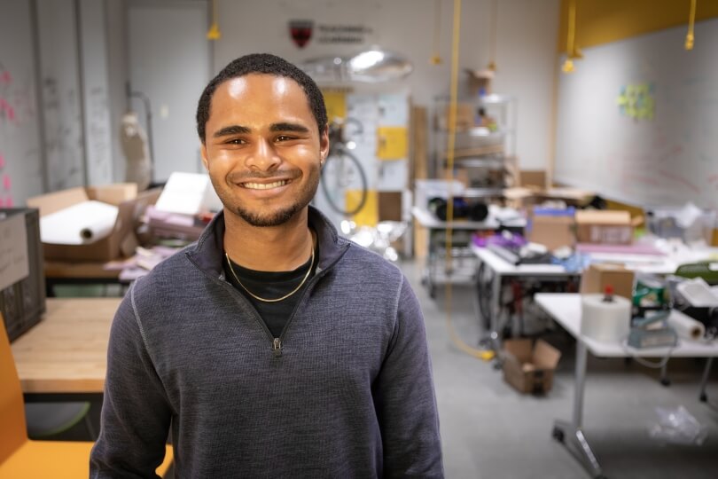 Harvard SEAS senior Adam Reid wearing a gray pullover in front of boxes and bicycle parts