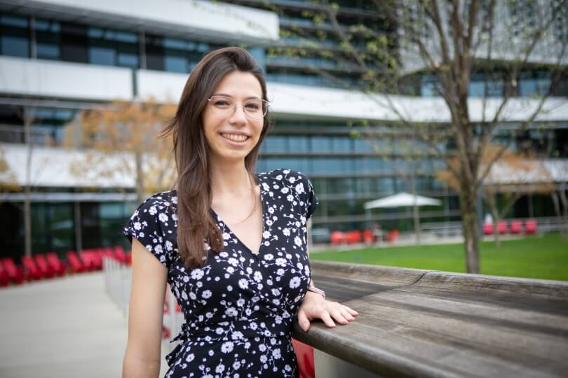 Harvard SEAS graduate student Maria Emilia Mazzolenis wearing a black and white dress standing in front of the Science and Engineering Complex next to a tree