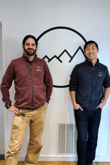 Harvard SEAS alumni Benjamin “Zags” Zagorsky and Kevin Fan in front of the logo for software company, Zagaran, Inc.