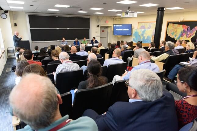 Four Harvard faculty sitting in front of a room filled with people sitting